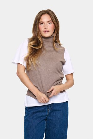 Béžový rolák z ľahkého pleteného materiálu, vrstvený nad bielou košeľou s krátkym rukávom. Model drží okraje, v kombinácii s modrými džínami.