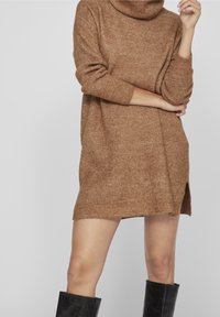 Vestito a maglia marrone con texture, dotato di ampio collo alto, maniche lunghe e spacchi laterali, progettato per una vestibilità comoda.
