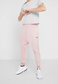 Grijze cropped T-shirt met wit logo en roze joggers met elastische tailleband, voorzien van zwart logo. Witte sportschoenen met zwarte accenten.