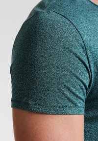 Teal short-sleeve shirt made from textured fabric with a heathered pattern. Features a crew neckline and clean stitch detailing.