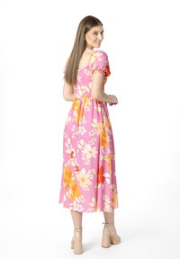 Il vestito midi floreale presenta uno sfondo rosa con fiori arancioni e bianchi, maniche a sbuffo e un corpino aderente, che arriva a metà polpaccio.