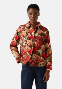 Kurtka z kwiatowym wzorem przedstawiającym czerwone i kremowe róże na zielonym tle, z kołnierzem i metalowymi guzikami, wykonana z miękkiego materiału.