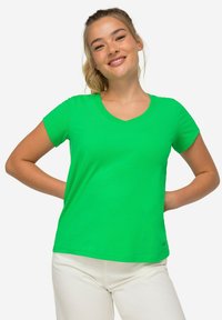 Zielona koszulka z dekoltem w serek, wykonana z miękkiego materiału, z krótkimi rękawami i dopasowanym krojem. Dodatkowym akcentem jest małe logo na dolnym brzegu.