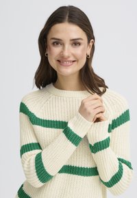 Pull en tricot couleur crème avec des rayures horizontales vertes, des poignets côtelés et un col rond, présentant un motif texturé.