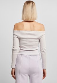 Schulterfreies Oberteil mit langen Ärmeln aus hellgrauem Rippstoff, figurbetontes Design, zeigt freien Rücken und Schultern, kombiniert mit helllila Hosen.