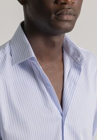 Camisa de vestir de rayas azul claro y blanca, fabricada en algodón, con cuello punta, botones visibles y una textura suave. Primer plano del escote y el cuello.