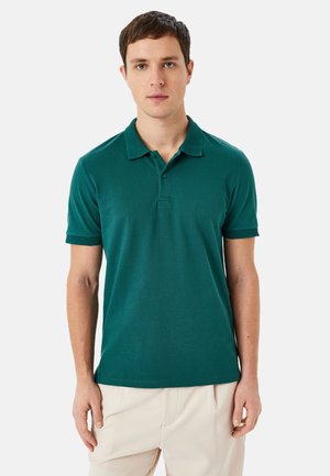 Polo shirt turchese con colletto testurizzato e maniche corte, realizzato in un tessuto liscio, abbinato a pantaloni chiari. Design minimalista.