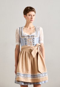 Traditionelles Kleid mit einem blauen Oberteil, das mit Spitzenärmeln und Korsett-Details ausgestattet ist, kombiniert mit einem beigen Rock, der in der Taille mit einer Schleife gebunden ist.
