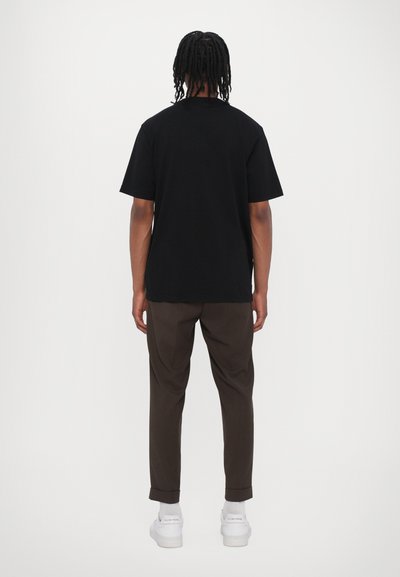 Tricou din bumbac negru, cu mâneci scurte, croi drept, purtat cu pantaloni maro și adidași albi. Material simplu, design minimalist.