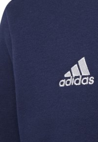 Sudadera azul oscuro hecha de una mezcla de algodón, con un logo de Adidas bordado en blanco en el área izquierda del pecho. Textura suave.