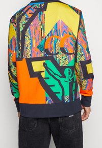 Sweat-shirt multicolore présentant des motifs complexes en vert, orange, jaune et bleu. Le design inclut des accents graphiques et un ourlet contrastant.