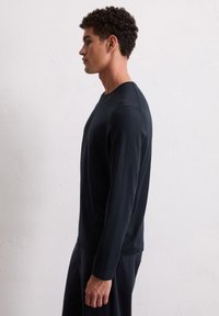 Langärmliges schwarzes Shirt aus weichem Stoff, mit einem Rundhalsausschnitt und lockerer Passform. Sanfte Textur mit minimalen Nahtdetails.