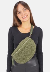 Sac en fausse fourrure vert en bandoulière avec une forme arrondie, fermeture éclair et surface texturée. Dispose d'une sangle en cuir vert.