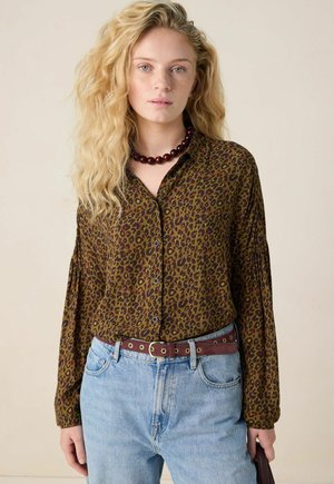 Bruin blouse met luipaardprint, met knoopsluiting en lange mouwen, gedragen met high-waisted lichtblauwe jeans en een bordeauxrode riem.