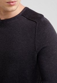 Maglione lavorato a maglia di colore grigio scuro con collo rotondo e polsini a coste, cuciture delle spalle visibili e finitura morbida e strutturata.