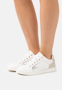 Vita sneakers med metalliska silver- och gulddetaljer, texturerad sidopanel, rund tå och snörningsdesign. Slät syntetiskt material.