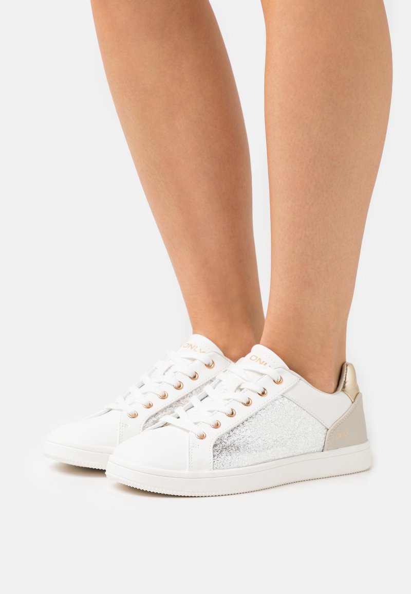 Vita sneakers med metalliska silver- och gulddetaljer, texturerad sidopanel, rund tå och snörningsdesign. Slät syntetiskt material.