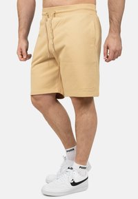 Shorts in misto cotone beige con vita elastica e cordoncino, dotati di tasche laterali e dettaglio del marchio ricamato sull'orlo.