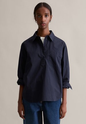 Granatowa koszula z zapięciem na guziki przy dekolcie, długimi podwiniętymi rękawami oraz kieszenią na piersi. Wykonana z teksturowanej tkaniny o luźnym kroju.