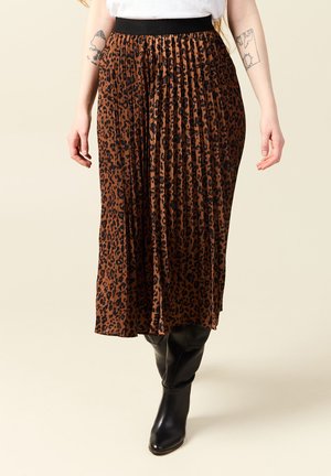 Jupe midi en imprimé léopard marron avec un design plissé et une taille élastique noire, associée à des bottes en cuir noir arrivant au genou.