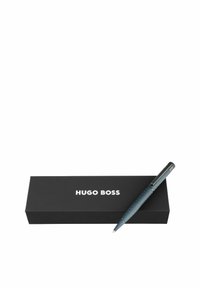 Stylo texturé bleu avec clip en chrome placé à côté d'une boîte noire avec l'inscription blanche "HUGO BOSS" sur le couvercle.
