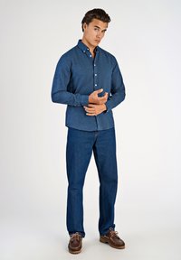 Camicia azzurra con bottoni e maniche lunghe, realizzata in tessuto strutturato. Indossata con jeans di denim scuro e mocassini marroni.