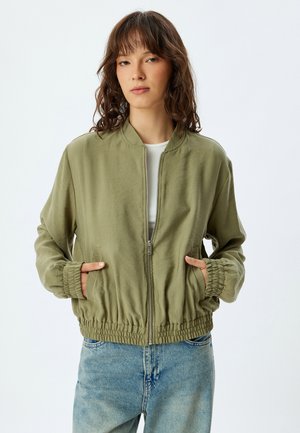 Chaqueta bomber verde oliva con cierre de cremallera en la parte delantera, puños elásticos y bolsillos laterales. Tejido ligero con un ajuste relajado y cintura con banda.