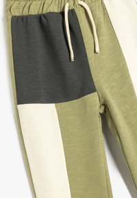 Joggers color bloqueados en verde oliva y gris oscuro con una textura ligera, cinturilla elástica y detalles en color crema. Cinta de ajuste ajustable.