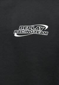 Μαύρη ζακέτα με λευκό λογότυπο που γράφει "REPLAY RACINGTEAM", με κομψή, λεία υφή και απλό, διακριτικό σχέδιο.