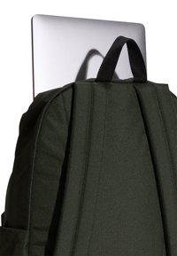 Tmavě zelený látkový batoh s polstrovanými stranami, vybavený černým horním popruhem z páskoviny a částečně zasunutým stříbrným notebookem.