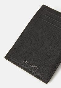 Černý kožený držák na karty s texturovaným povrchem, několika sloty na karty a jemným vyraženým brandingem "Calvin Klein".