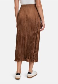 Jupe midi plissée marron avec une texture lisse et une taille élastique, associée à des baskets blanches avec des accents noirs.