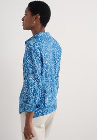 Blå mönstrad skjorta med blommönster i vitt, tillverkad av lättviktig tyg. Långa ärmar med uppvikta manschetter. Minimalistisk kragsdesign.