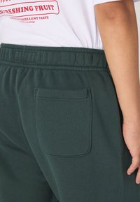 Dark green jogger pants made of soft fabric, featuring an elastic waistband, side pocket, and a smooth texture. Close-up view from the back.