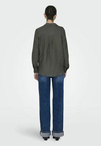 Dunkelgrünes, strukturiertes Hemd mit einem Rückensteg, kombiniert mit hochgeschnittenen blauen Jeans mit umgeschlagenen Säumen und einer lockeren Passform.