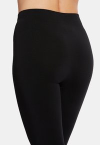 Zwarte leggings met een soepele, elastische textuur en een hoge tailleband, ontworpen voor comfort en pasvorm, die een slanke silhoutte laten zien.
