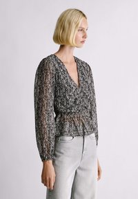 Čiernobiela blúzka s vzorom, hlbokým výstrihom do V, dlhými nafúknutými rukávmi a zúženým pásom; ľahká a polopriesvitná látka.