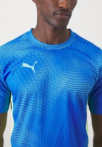 Blaues Sportshirt mit einem strukturierten Muster in verschiedenen Blautönen, mit Rundhalsausschnitt und einem weißen Logo auf der Brust.