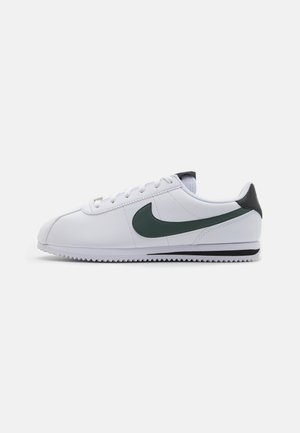 Zapatillas Nike blancas con un swoosh verde, acento negro en el talón y suela texturizada blanca. Cierre con cordones y un diseño liso y minimalista.