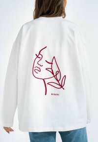 Witte oversized sweatshirt met een rood geborduurd gezicht en bladontwerp op de achterkant. Glad materiaal met een relaxte pasvorm en lange mouwen.