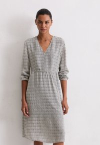 Schwarz-weißer, gemusterter Kleid mit V-Ausschnitt, langen Ärmeln und elastischem Taillenzug, das unter das Knie fällt. Texturierte Stoff.