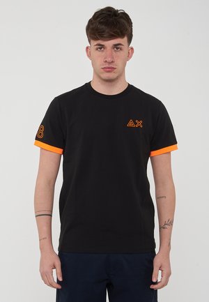 T-shirt nera in cotone con accenti arancioni sulle maniche e sui loghi. Presenta un collo rotondo e una vestibilità regolare. Design semplice con dettagli minimi.