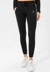 Čierne teplákové nohavice so slim fit strihom, sťahovacím pásom, bočnými vreckami a rebrovanými manžetami. Biele logo na ľavom boku.