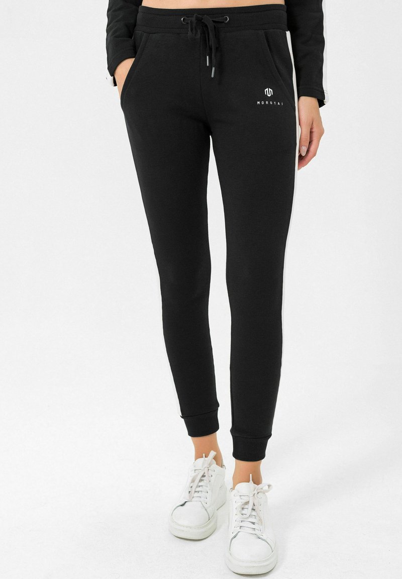 Čierne teplákové nohavice so slim fit strihom, sťahovacím pásom, bočnými vreckami a rebrovanými manžetami. Biele logo na ľavom boku.