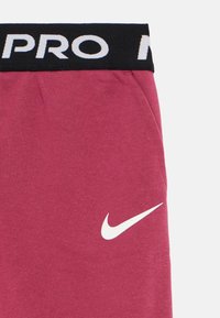 Spodnie dresowe Nike w głębokim odcieniu bordo. Wykonane z miękkiego materiału z czarnym elastycznym pasem, na którym znajduje się napis "PRO" w białym kolorze. Białe logo Nike po boku.