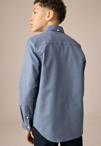 Camicia blu a maniche lunghe con colletto classico, dettagli con bottoni sui polsini e tessuto dalla texture liscia, con orlo posteriore dritto.