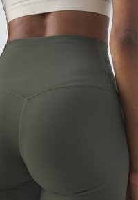 Legginsy z wysokim stanem w oliwkowym kolorze, wykonane z elastycznej tkaniny, z płaskimi szwami i bezszwowym paskiem, zapewniające gładką fakturę.