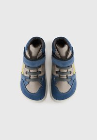 Une paire de baskets pour tout-petits bleues et grises avec des accents jaunes, des sangles Velcro et des lacets élastiques, sur un fond blanc uni.