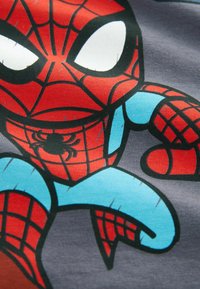 Pókember grafika szürke anyagon, élénk piros és kék színekkel, háló mintával és nagy, kifejező szemekkel.