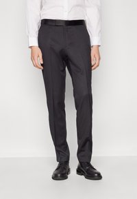 Calças ajustadas de cor cinza escuro com uma textura suave, apresentando um corte slim, e combinadas com um cinto preto. Acompanhadas de sapatos pretos.